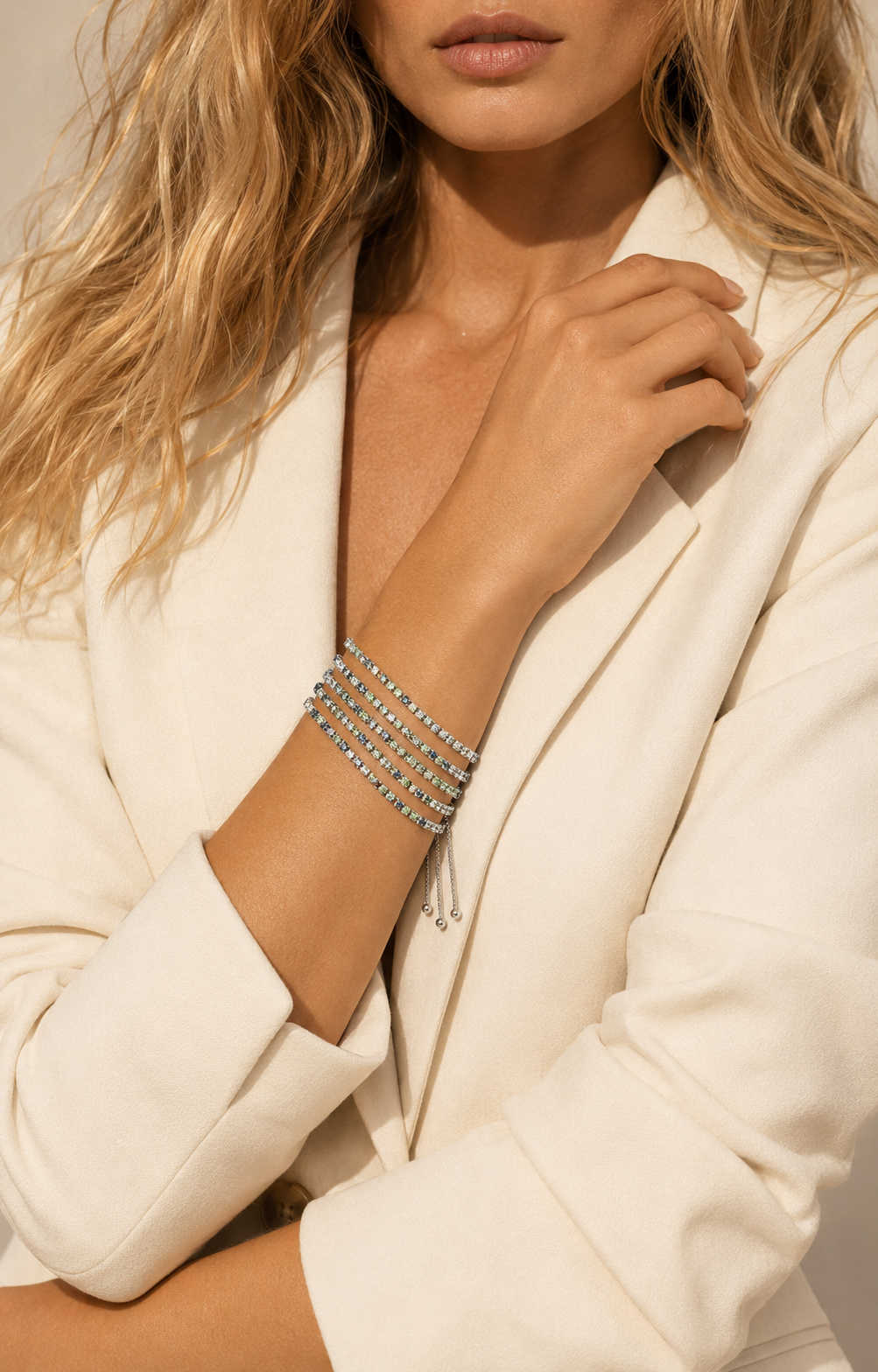 A close-up of a model wearing a stack of multi-strand silver beaded bracelets on her wrist, styled with a cream blazer.-