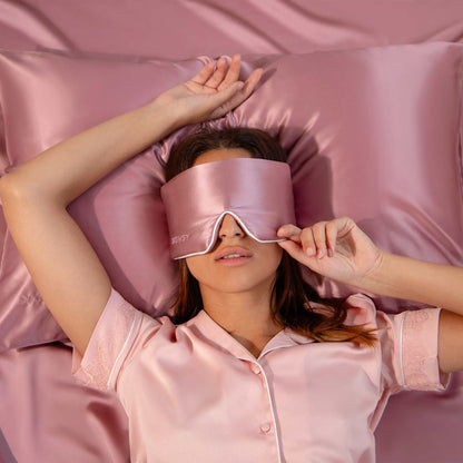 Model sleeping on pink Drowsy silk pillowcase with pink Drowsy silk sleep mask covering her eyes